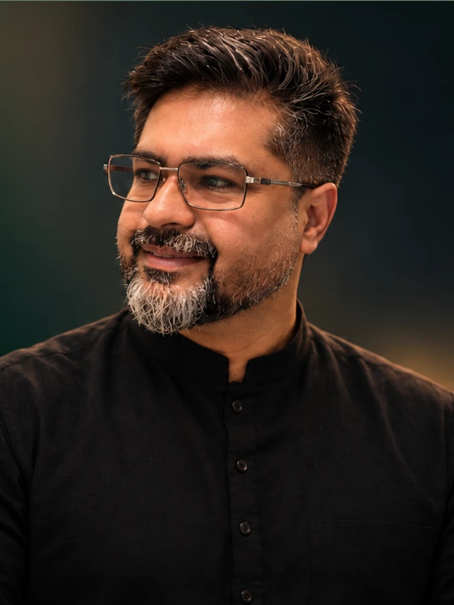Ahmed Umar Ali wearing a black shirt and jacket, looking toward the headline